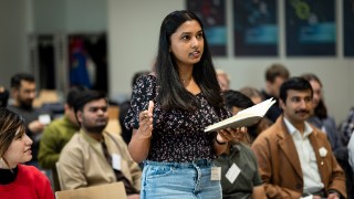 Frau mit Buch in der Hand steht im Publikum einer Green ICT-Veranstaltung und spricht